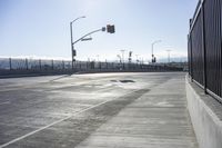 an empty intersection with a traffic light in the background and a fence around it on a sunny day