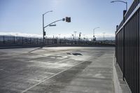 an empty intersection with a traffic light in the background and a fence around it on a sunny day