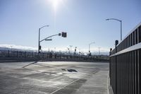 an empty intersection with a traffic light in the background and a fence around it on a sunny day