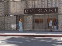 the woman is waiting for her bus outside of bvlgari boutiques at city street corner