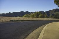 a paved street next to a cement wall and trees with mountains in the background at twilight