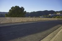 a paved street next to a cement wall and trees with mountains in the background at twilight