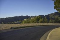 a paved street next to a cement wall and trees with mountains in the background at twilight