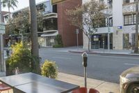 the view of a city street from a patio in the afternoon sunlight, showing a parking meter and a park bench