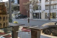 the view of a city street from a patio in the afternoon sunlight, showing a parking meter and a park bench