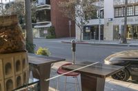 the view of a city street from a patio in the afternoon sunlight, showing a parking meter and a park bench