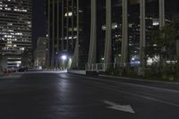 a very wide empty street at night near the tall building area of a city block