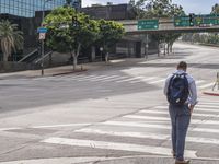 an officer stands near the sidewalk on an empty street as traffic passes below a bridge