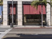 a street with a corner and palm trees in the background, some with red awnings and a stop light