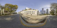 a city street and buildings is shown from a fish eye view lens while riding down it