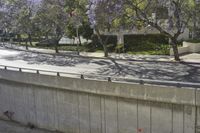 an empty roadway surrounded by several tall buildings and trees with purple flowers and green grass and fenced off parking lot
