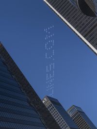 a plane flying in the sky above skyscrapers on a sunny day with jet trails written in the sky