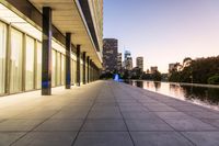 a long walkway next to a body of water surrounded by buildings at night time near the water