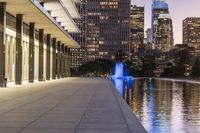 a long walkway next to a body of water surrounded by buildings at night time near the water