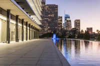 a long walkway next to a body of water surrounded by buildings at night time near the water