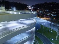 a curved walkway going over an elevated bridge in the evening with cars going down it