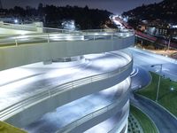 a curved walkway going over an elevated bridge in the evening with cars going down it