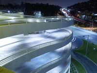 a curved walkway going over an elevated bridge in the evening with cars going down it