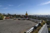 a man sits on the curb near a stop sign on a hill top overlooking a city