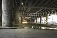the street below a bridge that leads to a car park at night, it's raining