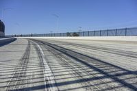 the empty road next to the fence is lined with a few snow patches and lines are visible