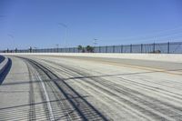 the empty road next to the fence is lined with a few snow patches and lines are visible