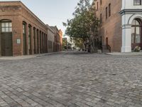 a view of a narrow alley that has a brick road on it and red building in the distance