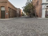 a view of a narrow alley that has a brick road on it and red building in the distance