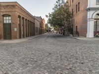 a view of a narrow alley that has a brick road on it and red building in the distance