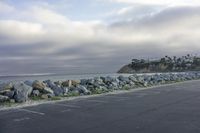 a man skateboarding along a rocky wall in a parking lot by the ocean on a cloudy day