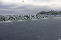 a man skateboarding along a rocky wall in a parking lot by the ocean on a cloudy day