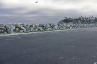 a man skateboarding along a rocky wall in a parking lot by the ocean on a cloudy day