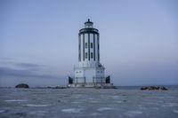 the small light house is white and gray next to the ocean water and rocks,