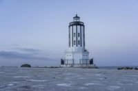 the small light house is white and gray next to the ocean water and rocks,