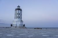 the small light house is white and gray next to the ocean water and rocks,