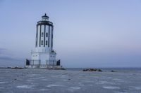 the small light house is white and gray next to the ocean water and rocks,