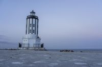 the small light house is white and gray next to the ocean water and rocks,