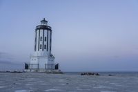 the small light house is white and gray next to the ocean water and rocks,