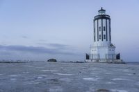 the small light house is white and gray next to the ocean water and rocks,