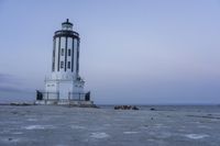 the small light house is white and gray next to the ocean water and rocks,