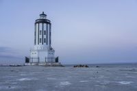 the small light house is white and gray next to the ocean water and rocks,