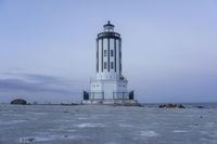 the small light house is white and gray next to the ocean water and rocks,