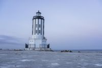 the small light house is white and gray next to the ocean water and rocks,