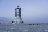 the small light house is white and gray next to the ocean water and rocks,