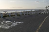 an empty road near a beach and waves as well as cars on the sand and houses on the beach