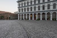 a large white building with arches in a brick courtyard in front of it in a city