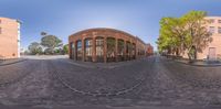 three view through a fish eye lens looking down a road at a building, which is surrounded by brick