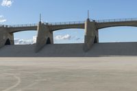 a concrete dam area with a train track bridge and concrete ramps in the background