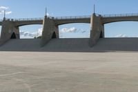 a concrete dam area with a train track bridge and concrete ramps in the background