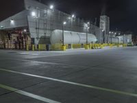 a factory with tanks at night time, in the background an industrial building with metal poles and overhead lighting